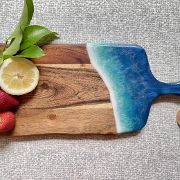 Tropical blue ocean resin paddle serving board on a background of light grey and white checks. Served with strawberries and lemon as decoration.